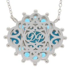 Silver pendant necklace with intricate design and blue accents, featuring a monogram in the center.