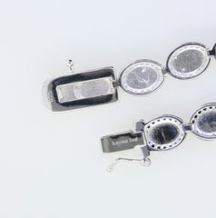 Close-up of a sterling silver tennis bracelet clasp with stainless steel tongue and cabochon settings for gemstones.