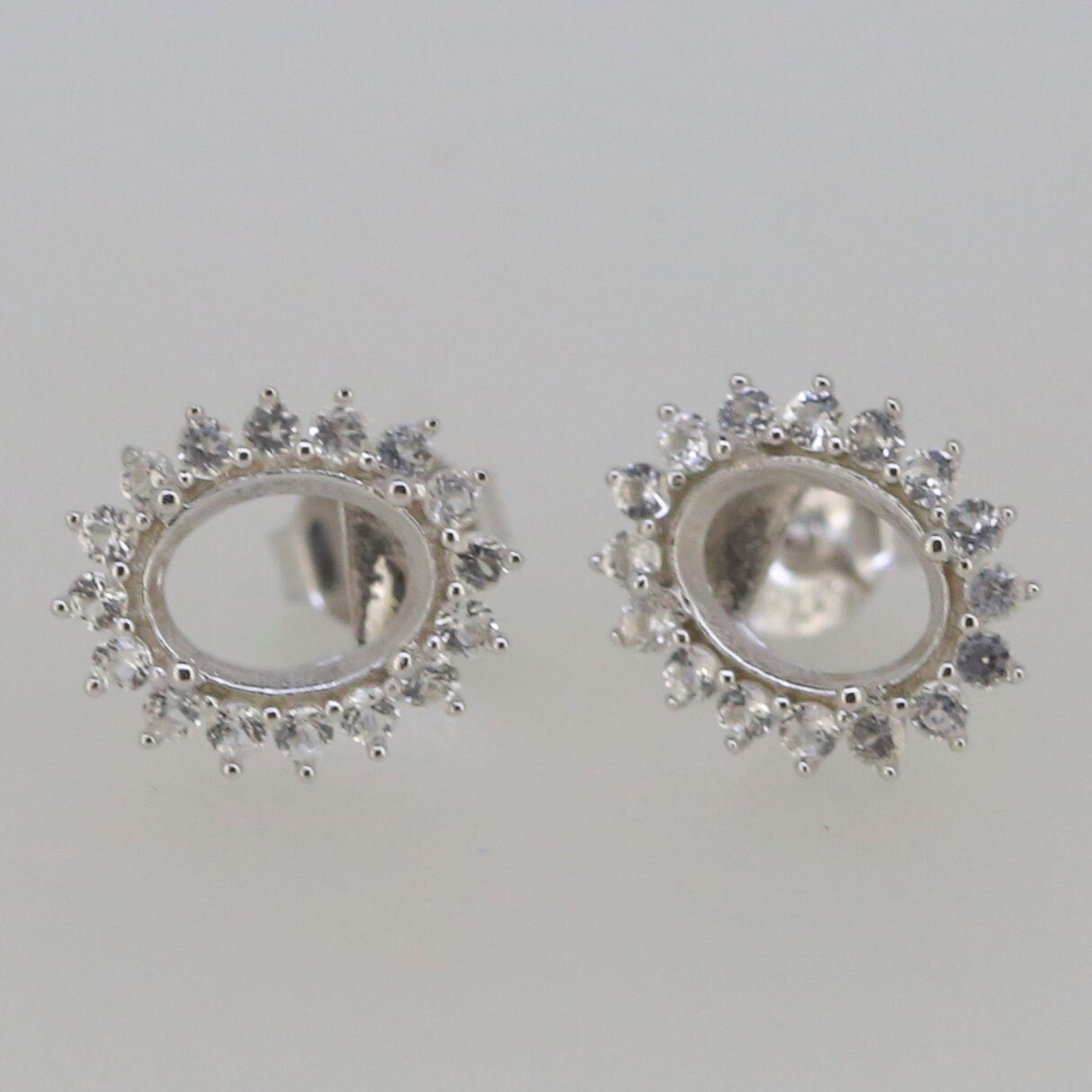 Sterling silver semi mount earrings setting with halo design for oval 8x6mm gemstones, featuring white topaz accent stones.