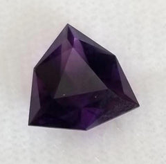 Faceted purple gemstone, resembling amethyst, showcasing intricate cuts and clarity on a light background.