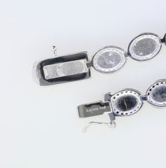 Close-up of sterling silver tennis bracelet clasp with stainless steel tongue and oval settings for gemstones.